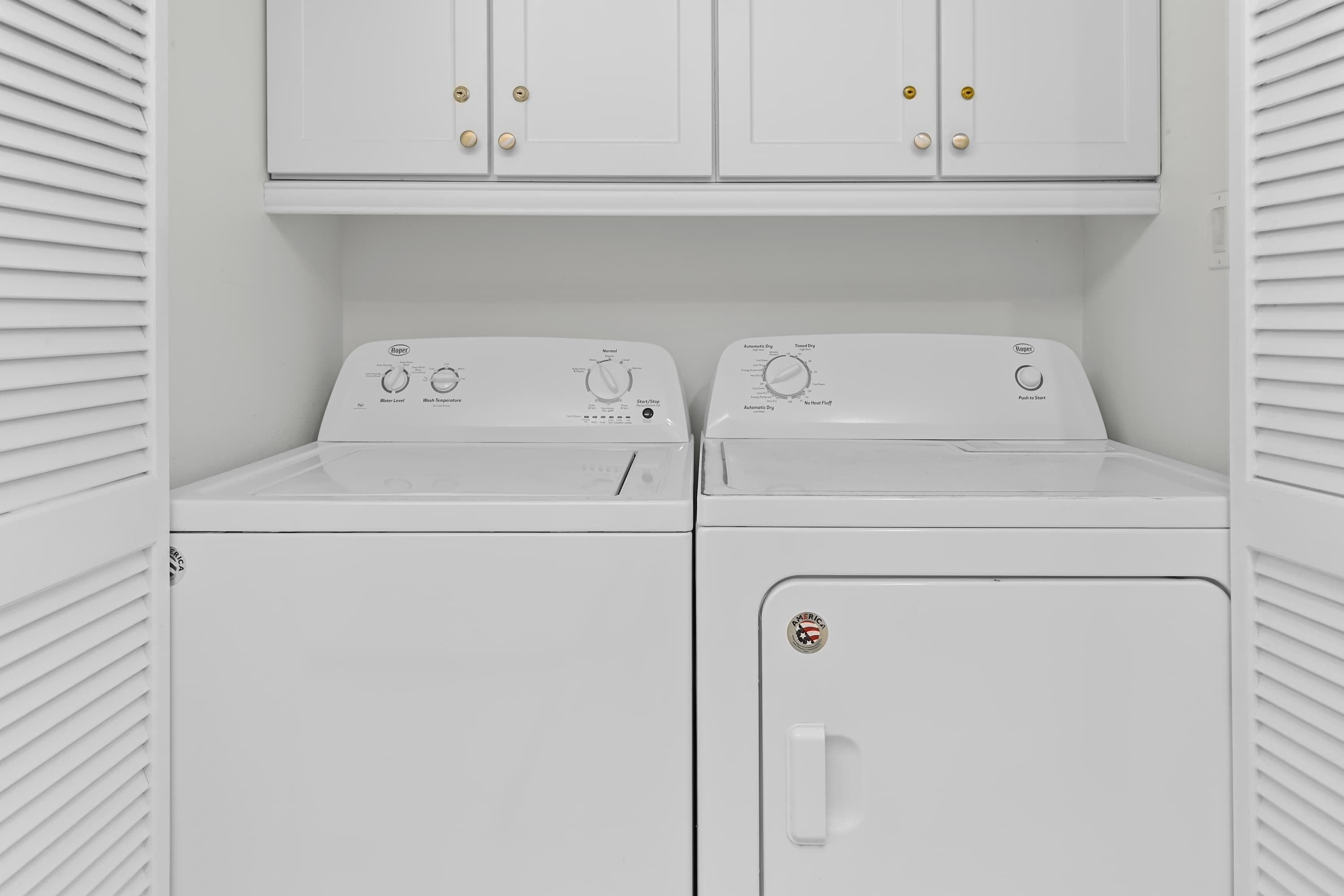 A laundry room with two front-loading washing machines and two cabinets above them.