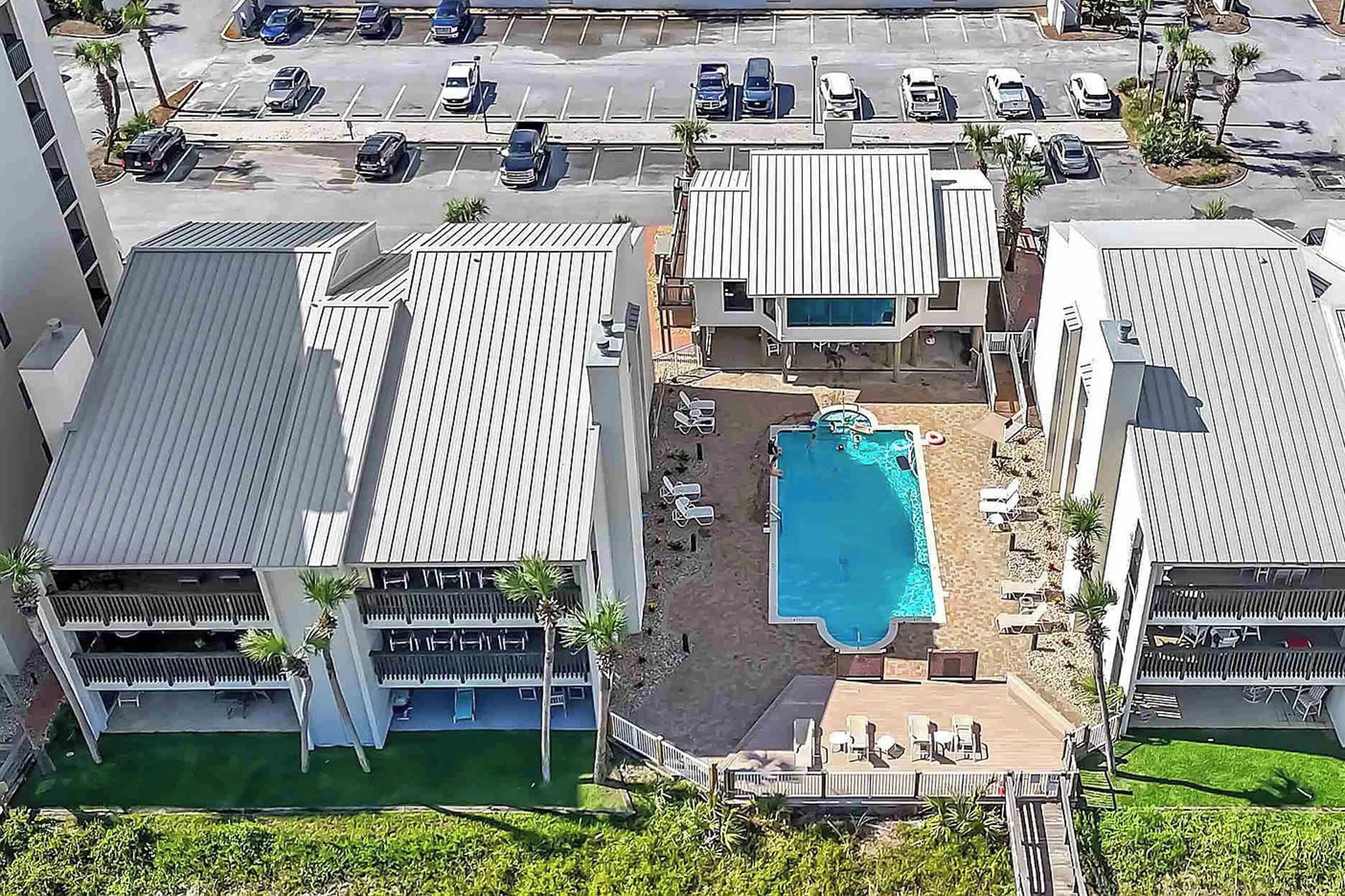 An aerial view of a hotel with a swimming pool, multiple parking spaces, and a landscaped area with palm trees.