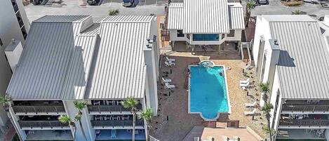 An aerial view of a hotel with a swimming pool, multiple parking spaces, and a landscaped area with palm trees.