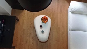 Una habitación con un sofá blanco, una lámpara de pie negra y una mesita con un frutero.