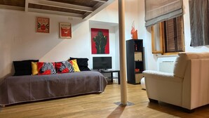 Una sala acogedora con un sofá, una cama con almohadones coloridos, un televisor y una estantería.