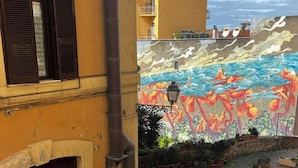 Un patio con un mural de escena marina, plantas en macetas y un camino de adoquinado.