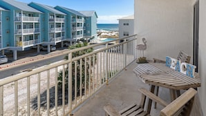 A balcony with a view of a beach and a pool, wooden furniture, and a swan decoration.
