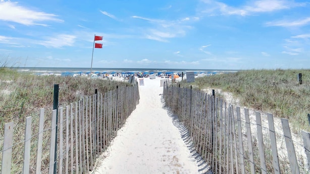 A sandy pathway leading to a beach area with a flag on a pole.