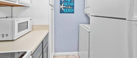 Een smalle keuken met witte apparaten, een magnetron en een koelkast. Een bord op de muur met de tekst: 'Het leven is beter aan het strand'.