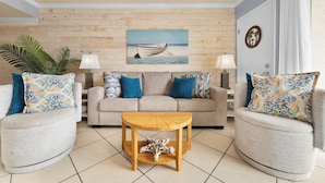 A living room with a wooden wall, a sofa, two armchairs, a coffee table, and a painting of a boat on the wall.
