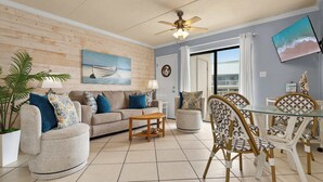 A living room with a sofa, armchairs, a glass dining table, and a ceiling fan.