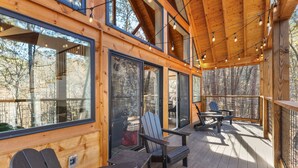 Une terrasse en bois avec des fauteuils Adirondack, de grandes fenêtres et des guirlandes lumineuses.