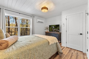 A bedroom with a large bed, a TV on a dresser, a window with a view of trees, and a white door. - Arcade | Private Hot Tub | Firepit | Fireplace | Close to Attractions (Sevierville)