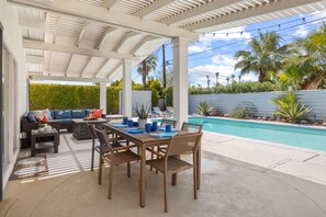 Um pátio externo com piscina, área de estar coberta e espaço para refeições.