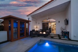 A modern outdoor living area with a pool, seating, and a glass-enclosed structure. - The Elemental Retreat- Pool Spa and Sauna (La Quinta)