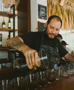Um barista a servir café em copos, com um aviso a anunciar passeios de café e cacau.
