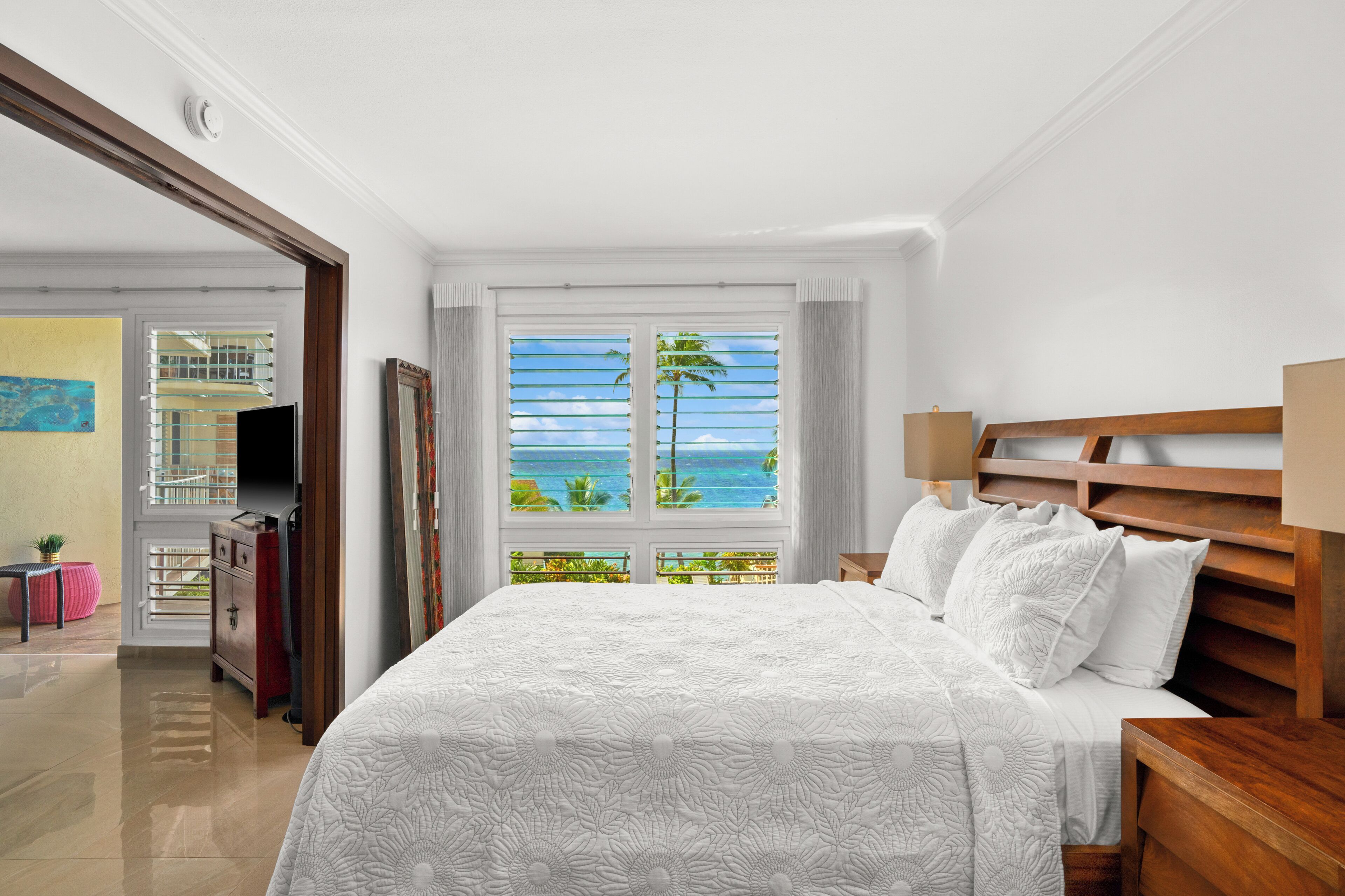 Un dormitorio con una cama grande, cabecera de madera, mesita de noche y ventana con vista al océano.