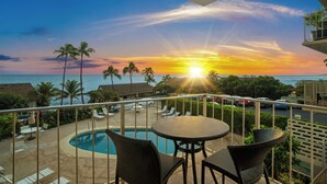 Un balcone con vista sul tramonto sull'oceano, una piscina e un'area relax all'aperto.
