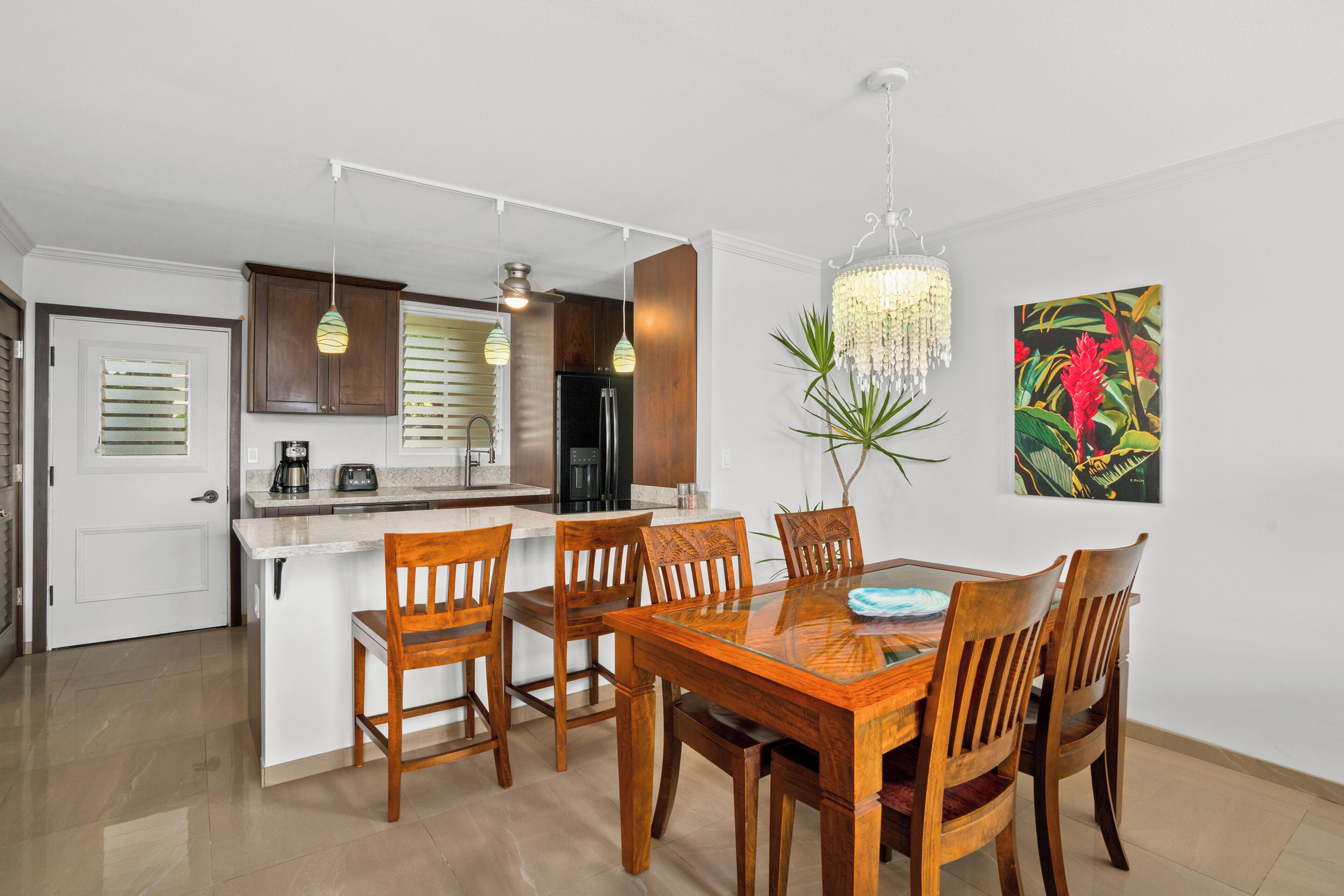 Una cocina moderna con armarios blancos, una isla central y una zona de comedor con sillas de madera y una mesa de vidrio.
