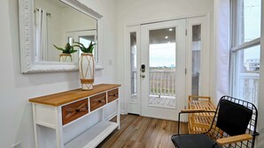 Una habitación con una consola blanca, un espejo, una puerta que da a un balcón y una silla negra.