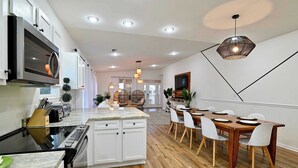 Una cocina moderna con armarios blancos, una isla central y un comedor con mesa de madera y sillas blancas.