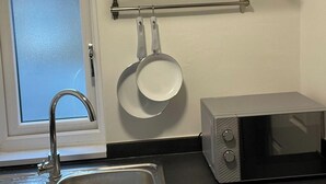 A kitchen with a stainless steel sink, a microwave, a window with frosted glass, and a shelf with pots and pans. - Hackney E5 - Perfect for Couples Getaway (London)