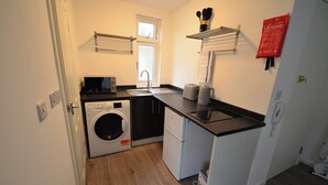 A compact kitchen with a washing machine, a refrigerator, and a microwave. - Hackney E5 - Perfect for Couples Getaway (London)