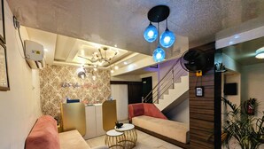 A modern lobby with a sofa, a round coffee table, a chandelier, and a staircase. - The Vibs International (Damoh)
