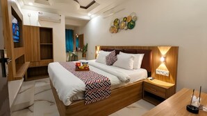 A modern hotel room with a large bed, wooden headboard, bedside tables, and a TV mounted on the wall. - The Vibs International (Damoh)