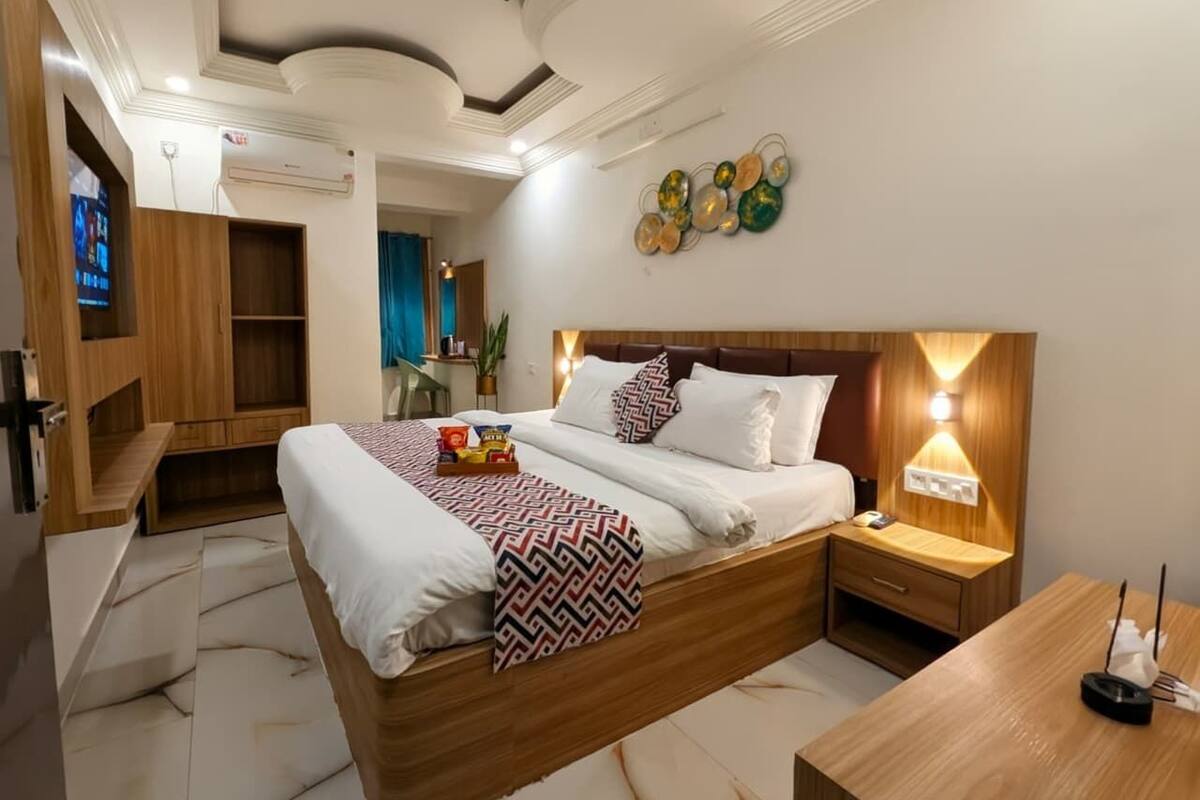 A modern hotel room with a large bed, wooden headboard, bedside tables, and a TV mounted on the wall.
