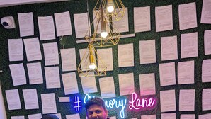 Two individuals standing in front of a wall covered with papers and a neon sign that reads "#Chicory Lane". - The Vibs International (Damoh)