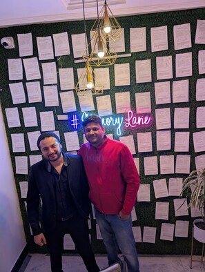 Dos personas frente a una pared cubierta de papeles y un letrero de neón que dice '#Chicory Lane'.