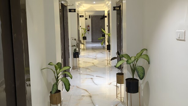 A hallway with marble flooring, potted plants, and doors labeled with room numbers. - The Vibs International (Damoh)