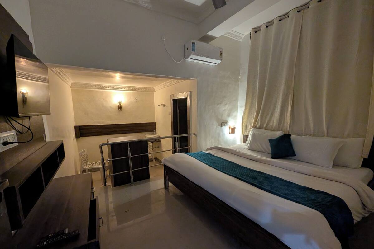 A hotel room with a bed, a desk, a chair, and an air conditioning unit.