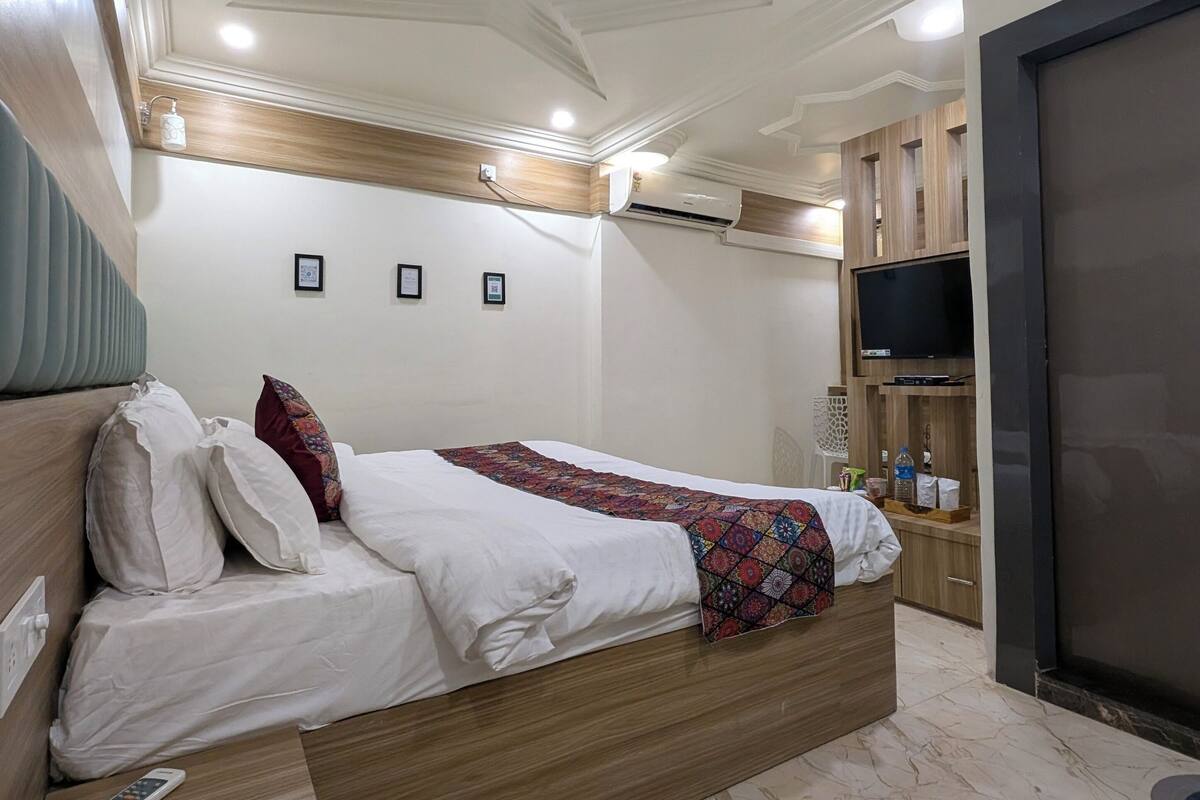 A modern bedroom with a bed, wooden headboard, ceiling fan, air conditioning unit, and a TV on a stand.