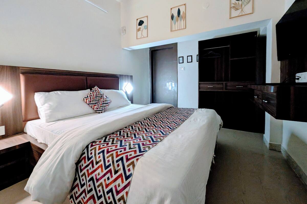 A hotel room with a large bed, a wooden headboard, a wardrobe, and a flat-screen TV.