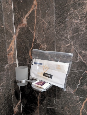 A bathroom with a marble wall, a toothbrush holder, a toothbrush, and a dental kit bag.