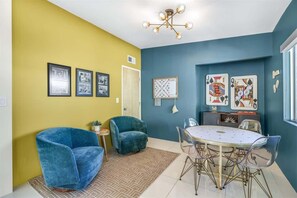 Un coin repas comprenant une table ronde et des chaises, un fauteuil bleu et une petite table d’appoint avec une plante.