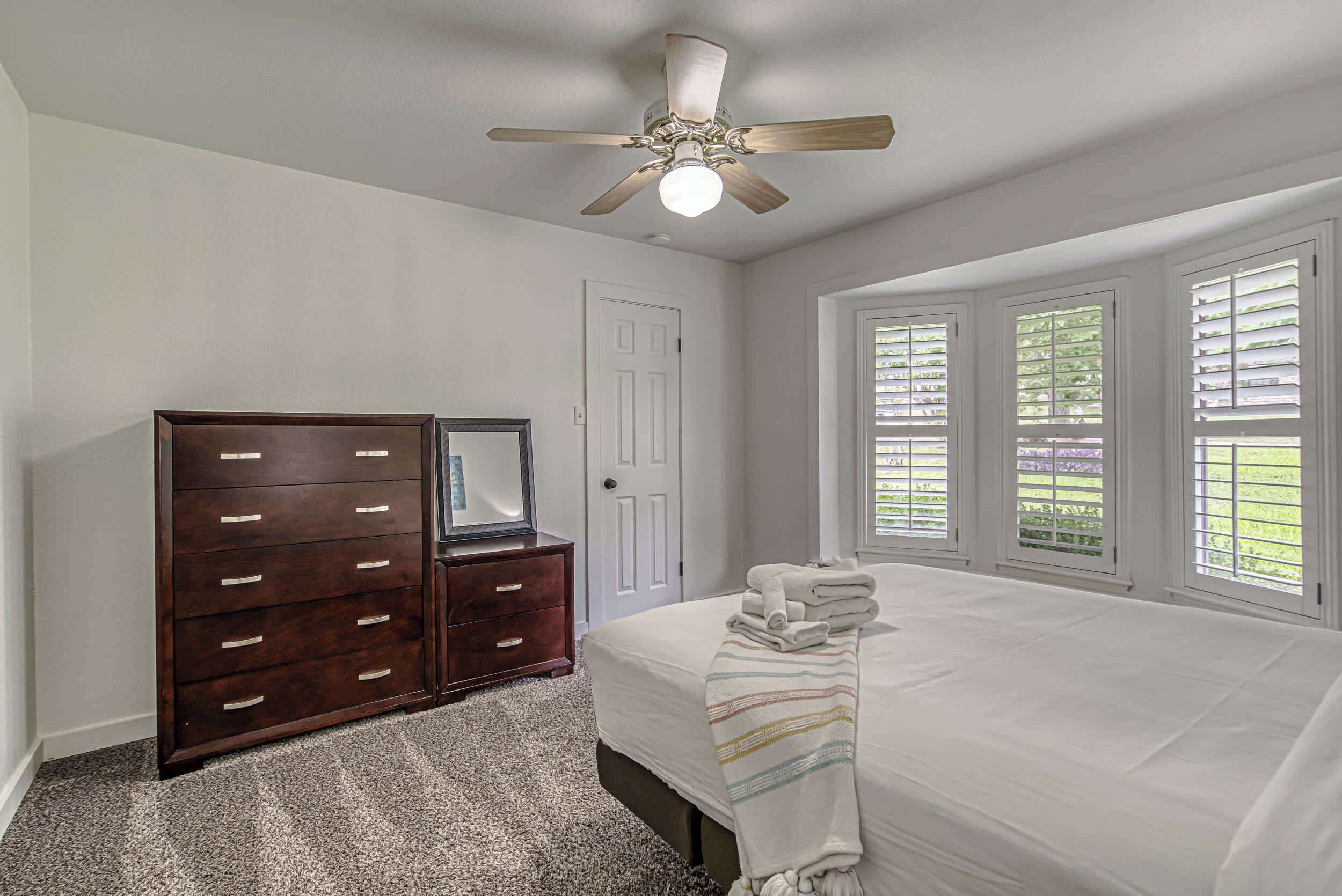 A bedroom with a bed, a dresser, a ceiling fan, and a window with blinds.