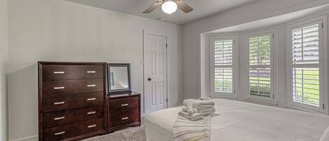 A bedroom with a bed, a dresser, a ceiling fan, and a window with blinds.