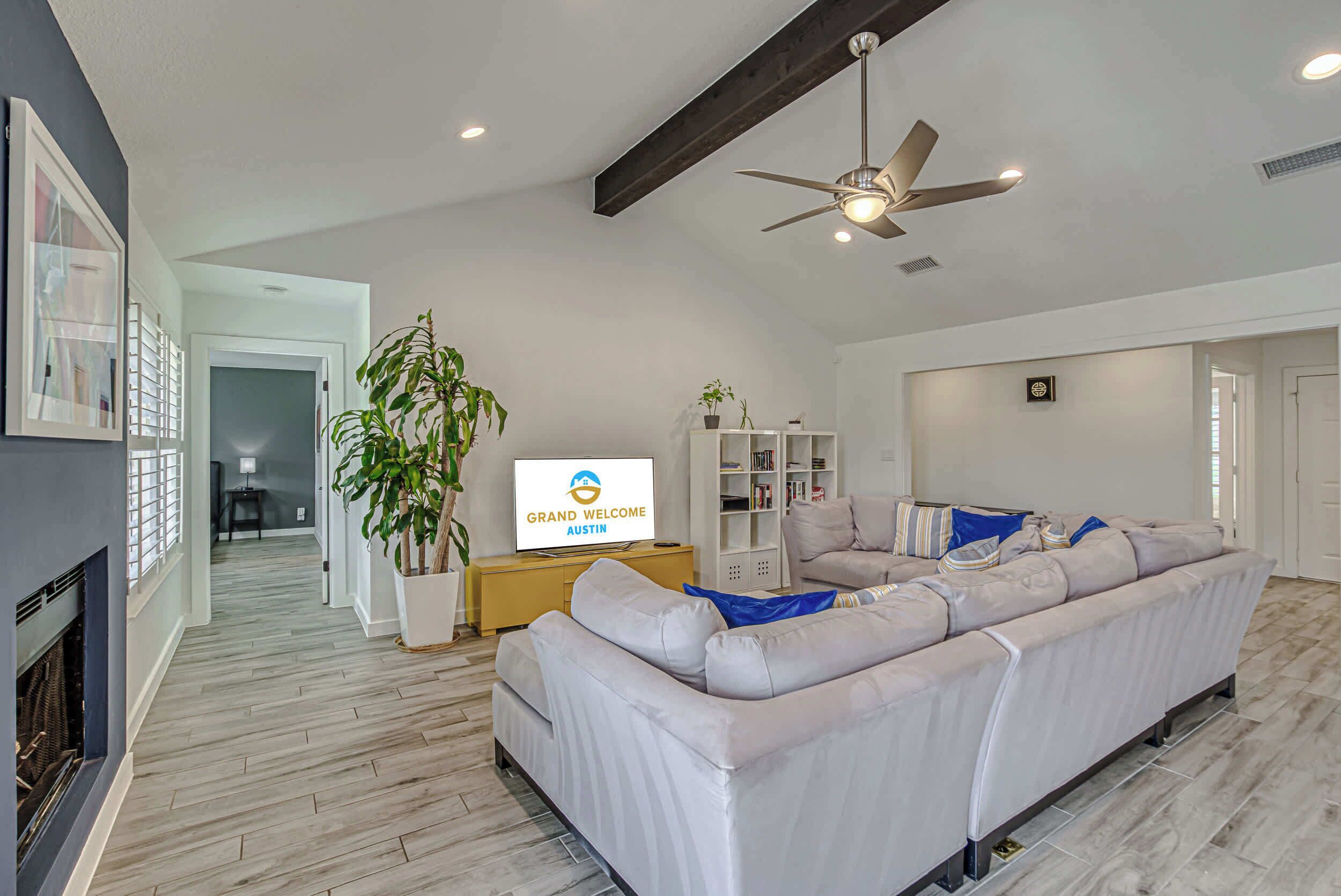A modern living room with a sectional sofa, a flat-screen TV, a ceiling fan, and a fireplace.