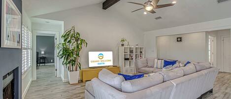 A modern living room with a sectional sofa, a flat-screen TV, a ceiling fan, and a fireplace.