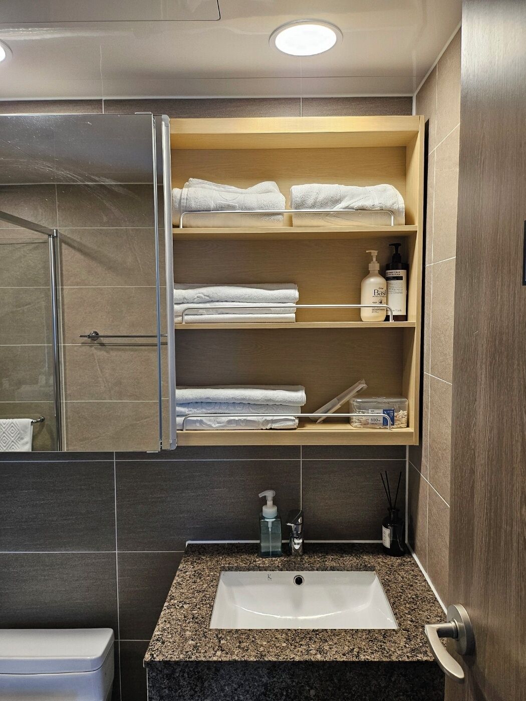 A bathroom with a built-in shelf holding towels and toiletries, a sink with a faucet, and a shower area.