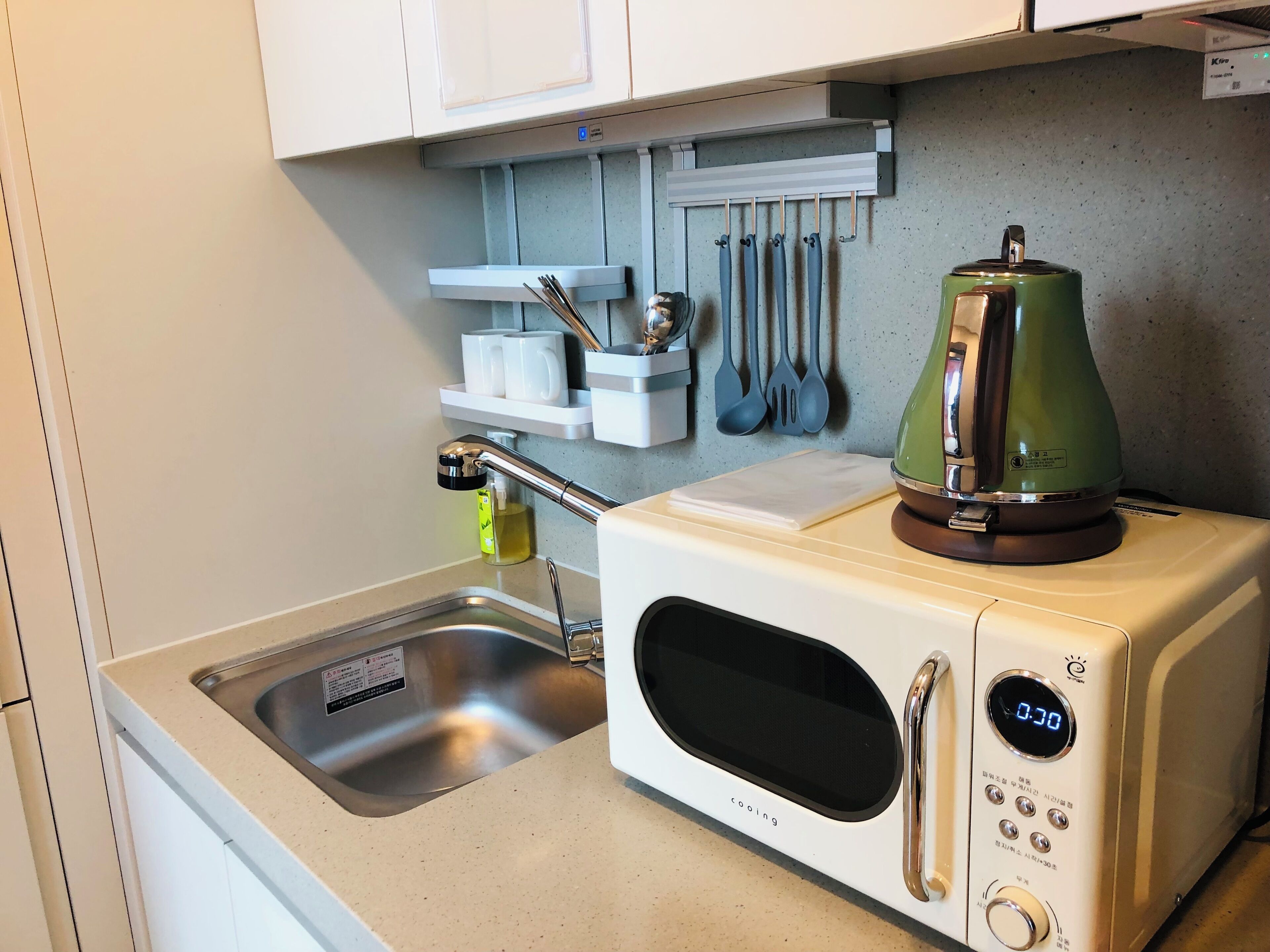 Een kitchenette met een magnetron, waterkoker en keukengerei dat aan de muur hangt.