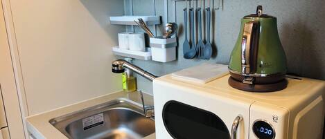 A kitchenette with a microwave, kettle, and utensils hanging on the wall.