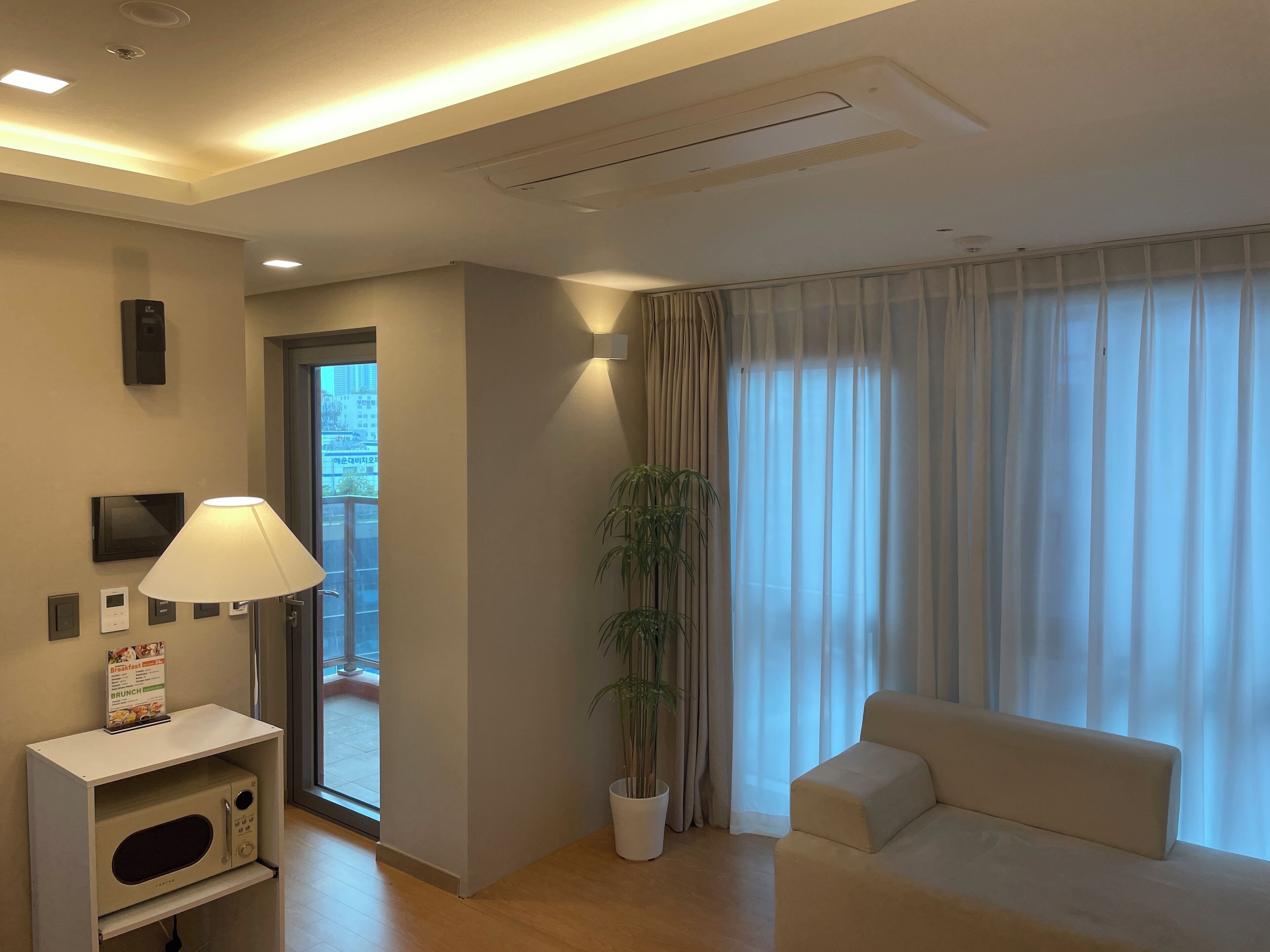 A modern living room with a sofa, a lamp, a potted plant, and a microwave on a stand.