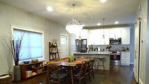 Une cuisine moderne avec des meubles en bois, des appareils électroménagers en acier inoxydable et un coin repas comprenant une table et des chaises en bois.