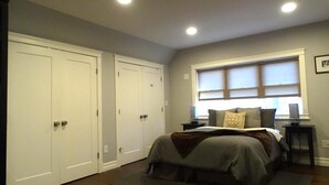 A bedroom with a large bed, two wardrobes, a window with blinds, and a desk with a lamp. - Park-Side Home in Jamaica Plain (Boston)
