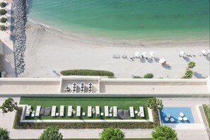 Vista aerea di un resort sulla spiaggia, con spiaggia sabbiosa, lettini, ombrelloni e area piscina.