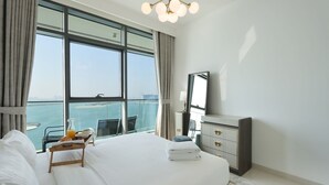 Camera d'albergo con un letto grande, una scrivania con sedia, un comò e una grande finestra con vista sul mare.