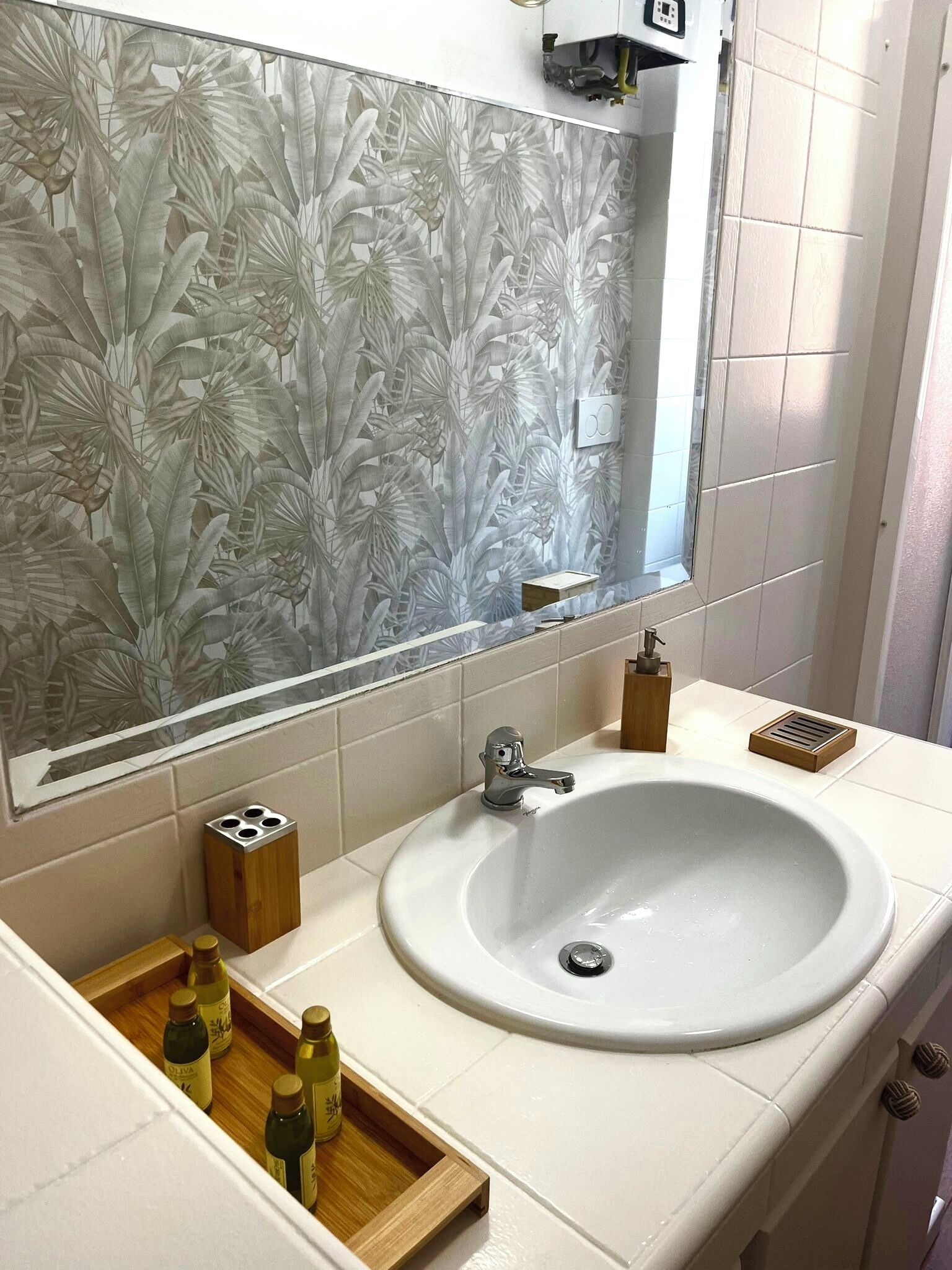 A bathroom with a white sink, a mirror, and a decorative wall with a leaf pattern.