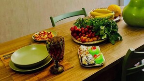 Une table à manger avec des assiettes remplies de nourriture, un verre contenant une boisson et une poire verte. On y voit également des étagères avec des plantes et un cactus.