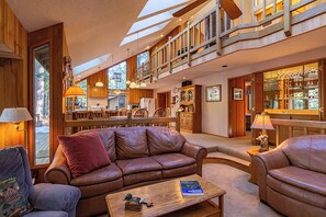 Un'ampia zona giorno con soffitto alto, arredi in legno e una sala da pranzo visibile sullo sfondo.