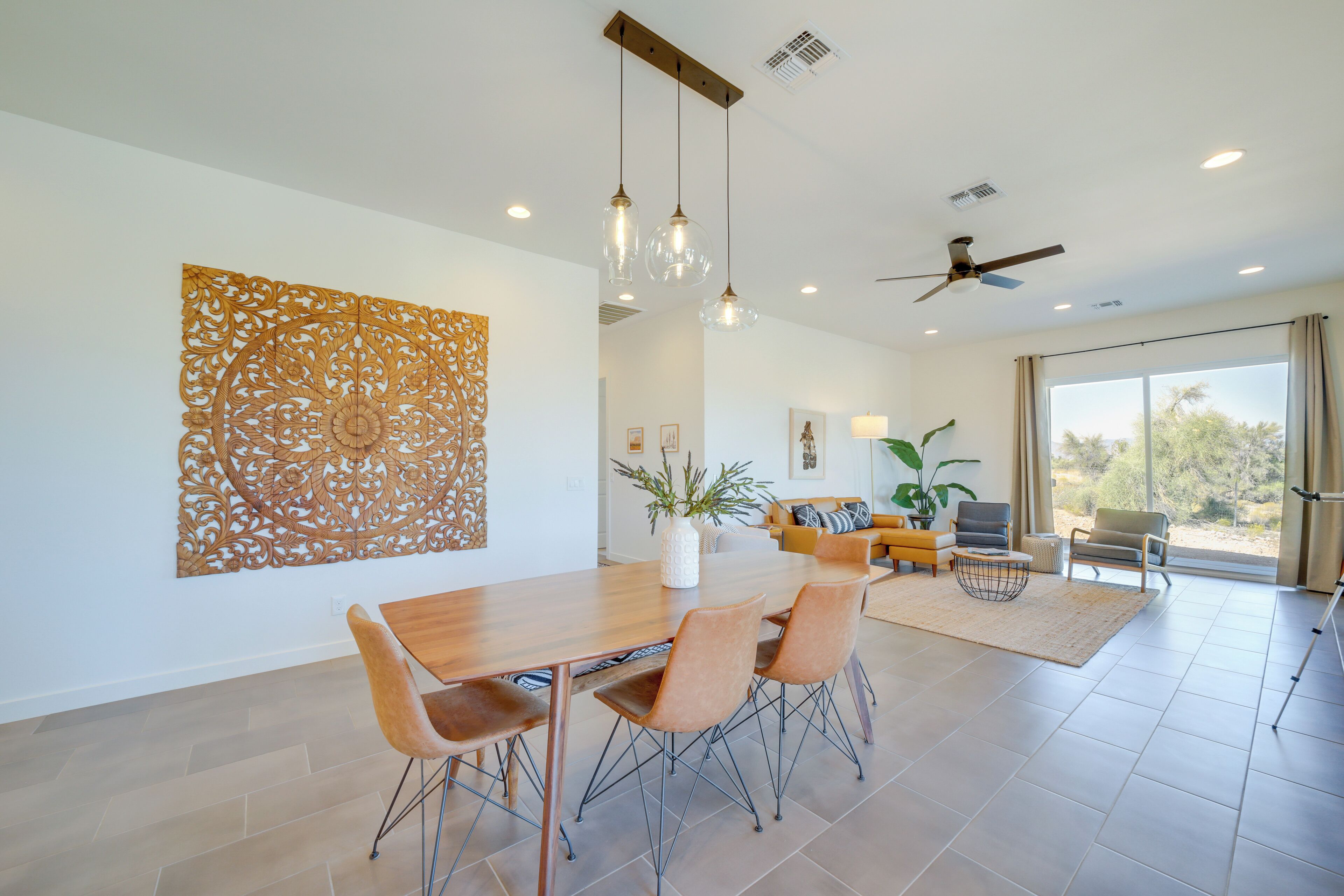 A spacious dining area with a wooden table and chairs, a decorative wall piece, and a ceiling fan.